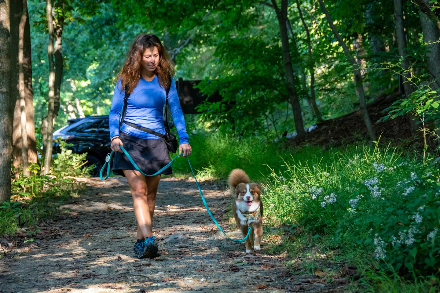 Woman walking a dog on a wooded trail.