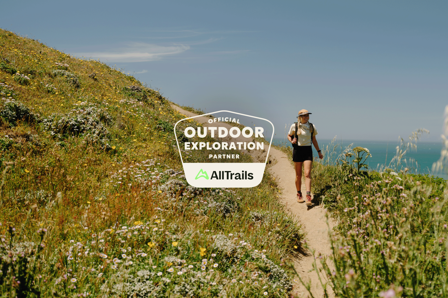 Woman hiking on a coastal trail, surrounded by wildflowers and ocean views.